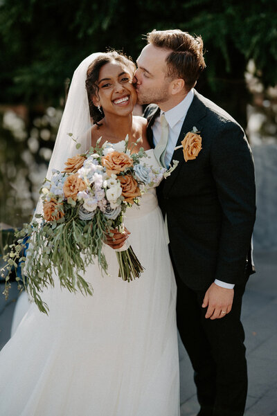 A bride and groom smile joyfully during their wedding, the bride holding a colorful bouquet.