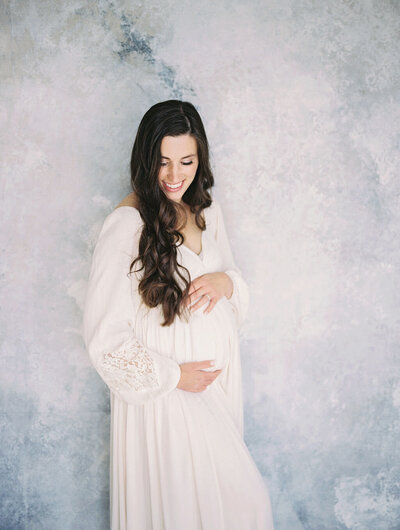 Richmond maternity photographer | Film image of a pregnant mother in a white dress holding her belly as she looks down and smiles by Jacqueline Aimee Portraits