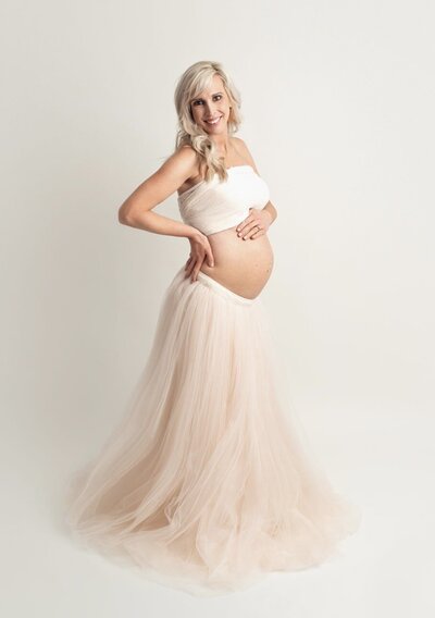 Pregnant mother wearing a bandeau cream top and light pink skirt showing pregnant belly.