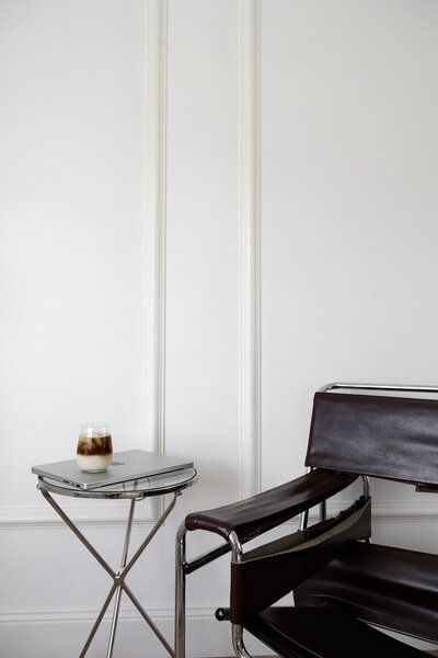 Minimalist corner with a leather chair, small round side table, and candle against a white paneled wall