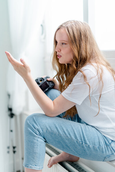 Vrouwelijke fotograaf in actie met camera in haar hand op een vensterbank. Portretfotograaf Isabeau Bosscher.