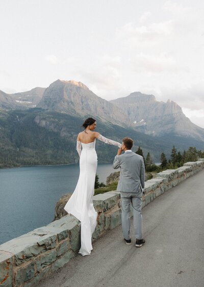 Bride and groom walking on a mountain road overlooking a lake.