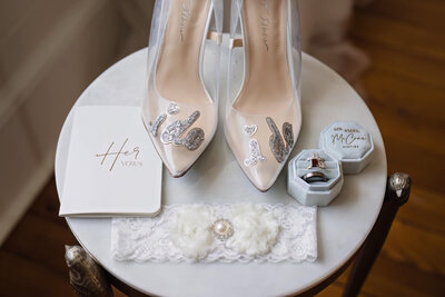 Elegant bridal shoes, vow book, and wedding rings arranged for a luxury wedding in Raleigh, NC.