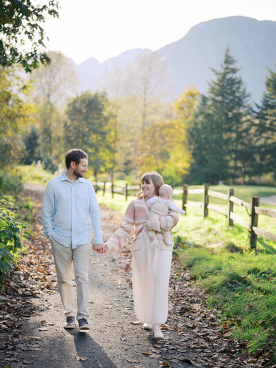 Mother holding a newborn while walking holding hands with her spouse