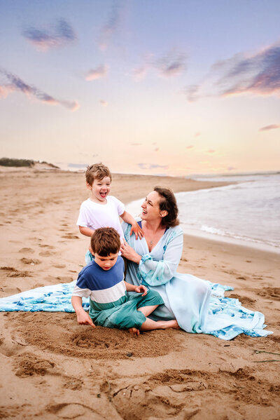 Mother in light blue gown at the beach sitting with her two young boys
