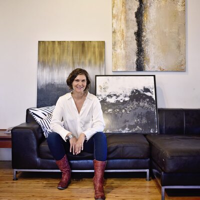 woman sitting on couch next to painting smiling
