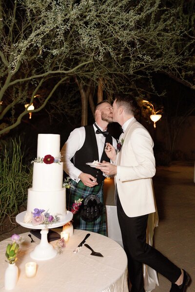 Two grooms kiss after cutting their wedding cake