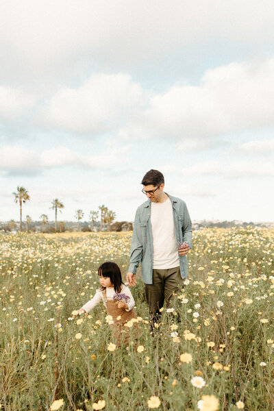 Father bending down to kiss daughter in golden field with wildflowers in Southern California