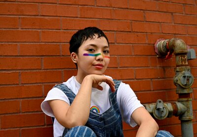 lesbian teen sitting against a brick wall with a rainbow stripe on her face