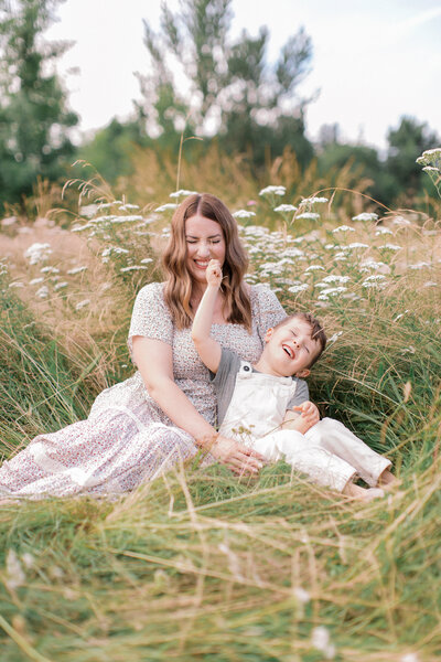 child tickles mom with grass while cuddling together on the ground