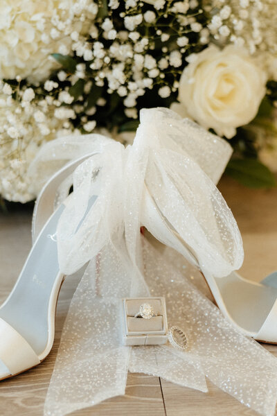 A bride's engagement ring in a ring box in front of her Christian Louboutin shoes.