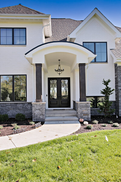 A detailed close-up of the front entry of a massive white mansion with striking black trimmings. This elegant design highlights the luxurious and modern architecture of the home, showcasing the grandeur of its entrance.