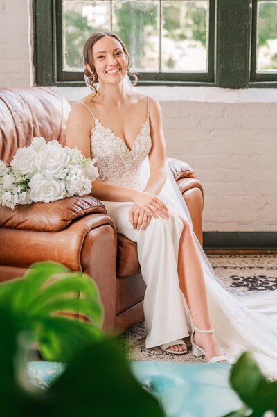 A gorgeous brunette bride sitting in a warm leather couch at The Woolen Mill during her bridal portrait session by JoLynn Photography, a destination wedding photographer