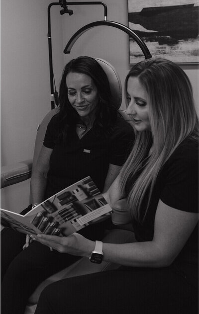 A black and white photo of Kylee and one of her employees are looking at a medical magazine.