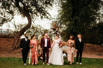 A bride and groom along with their 2 bridesmaids and 2 groomsmen are walking in a line and smiling at each other