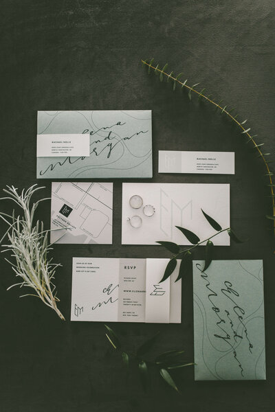 Flat lay of wedding stationery with envelopes and greenery.