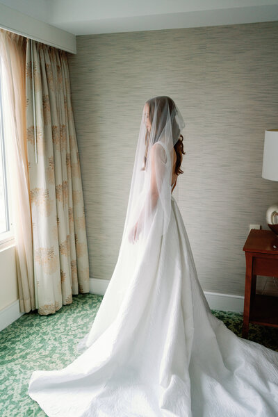 bride standing in all white wedding gown with veil covering face
