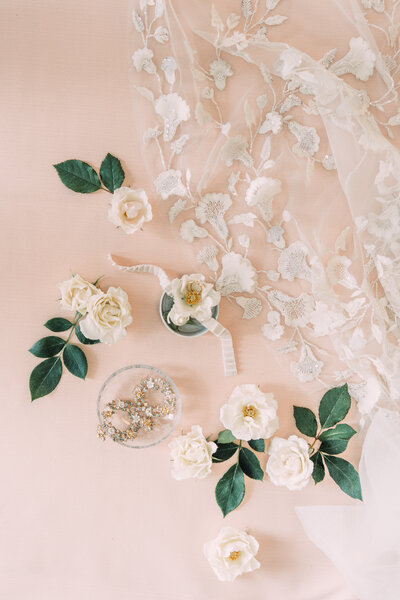Pink & white flatlay of Alexandra Grecco floral veil with fresh majolica roses, greenery, J Crew earrings, and wedding rings