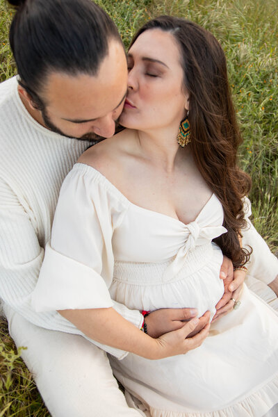 Woman kissing husband's cheek with both their hands on belly | Maternity Session