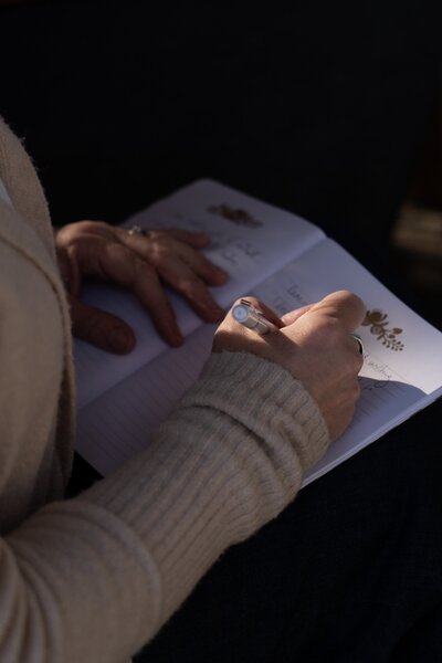 woman wearing a light tan sweater writing in a journal