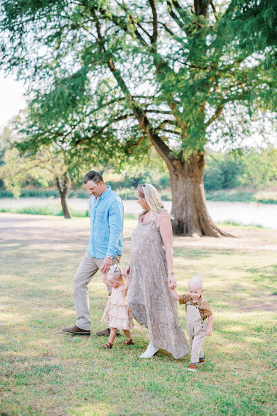 Portrait of parents and their two little children holding hands and walking together through the grass
