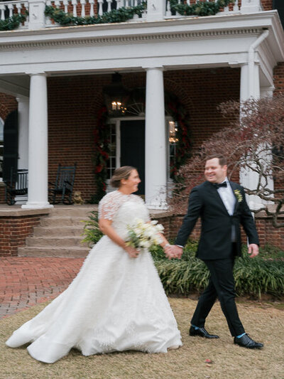 A bride and groom walking in front of an estate in Atlanta hand in hand, smiling at each other. The couple is slightly out of focus with a bit of motion blur giving a sense of movement. 