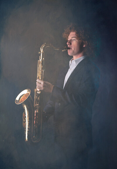 senior-boy-playing-saxaphone-in-studio-arlington-tx-with-smoke-in-a-suit