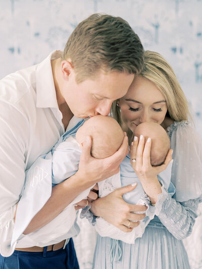 Blond mother and father bring their newborn twins up to kiss during their Chevy Chase newborn session, photographed by Marie Elizabeth Photography, Newborn Photographer Maryland.