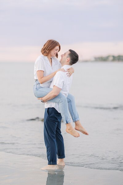 Groom picking up and kissing bride in the waves