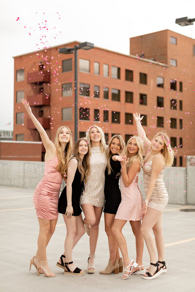 Six high school seniors throwing confetti into the air while smiling and standing on a garage rooftop in a city.