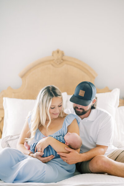 Portrait of couple sitting on a bed and holding their newborn baby