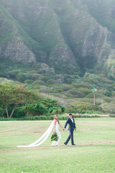 newlywed couple walking in front of the grand mountains of Kualoa Ranch also known as Jurassic Park