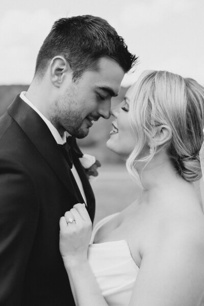 Black and white photo of bride pulling groom by his lapel towards her for a kiss