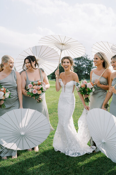 Bride and bridesmaids laughing with parasols