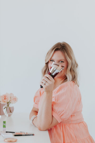 playful-makeup-artist-portrait-holding-makeup-brushes-at-vanity-the-frame-charlotte
