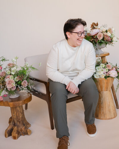 A person sitting in a chair smiling with plants on stools around them