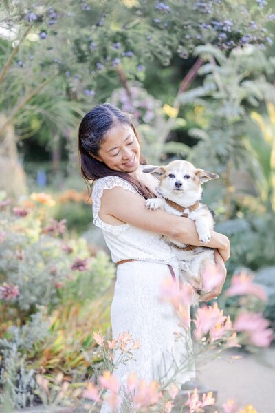 A cute little dog posing with her owner for the camera in front of beautiful spring flowers during a family photoshoot at Palo Alto