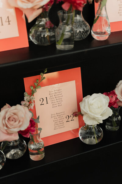 Hot pink seating chart table numbers sitting on a black shelf featuring flowers and full service design from Life in Letters