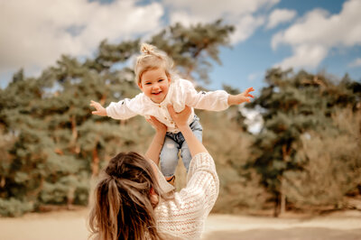 Mama laat dochter vliegen in de lucht en dochter lacht naar de camera terwijl ze haar armen spreid als een vliegtuin bij Herperduin