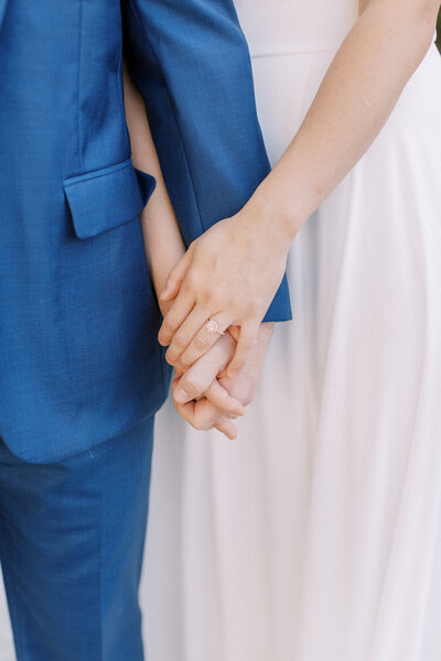 close up of bride and groom hands blue suit