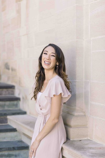 wedding photographer in pink dress leaning against wall