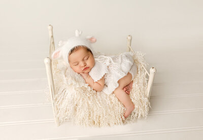 Newborn baby sleeping on their side with hands tucked under chin, styled with neutral fabrics in a fine-art studio setting.