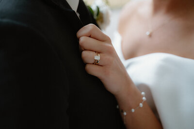 elegant wedding photo of bride holding onto her groom's jacket while showing off her wedding ring