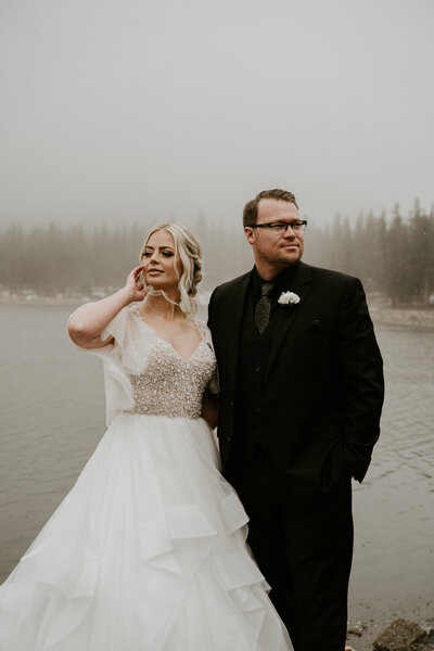 Couple in wedding attire pose beside foggy lake during Breckenridge mountain elopement.