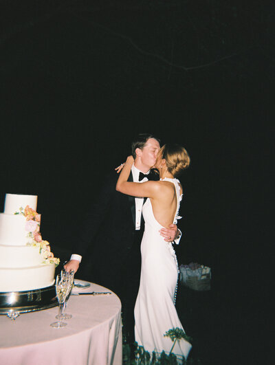 Flash film photo of bride and groom kissing with wedding cake in the foreground