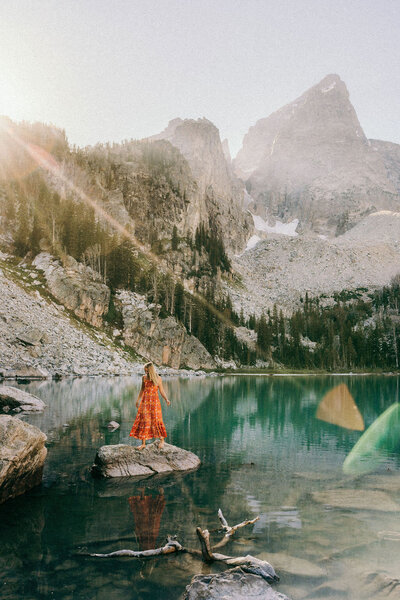 woman standing on a rock in a lake with mountains in the background