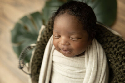 Newborn baby wrapped in a tan swaddle smiles in his sleep.