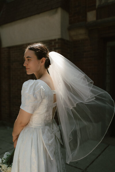 Bride in a vintage-inspired wedding dress with a flowing veil, photographed outdoors by Rainstorm Photo & Video with natural light and a cinematic, timeless feel.