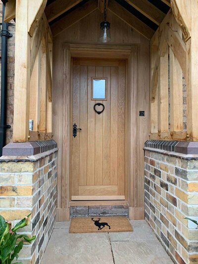 Wooden front door with a small window and heart-shaped decoration under a timber porch.