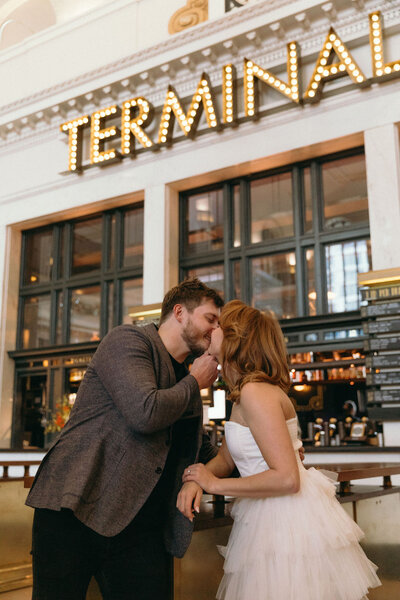 Couple kissing while leaning on a table inside the Union Station Terminal during their winter engagement photos. 
